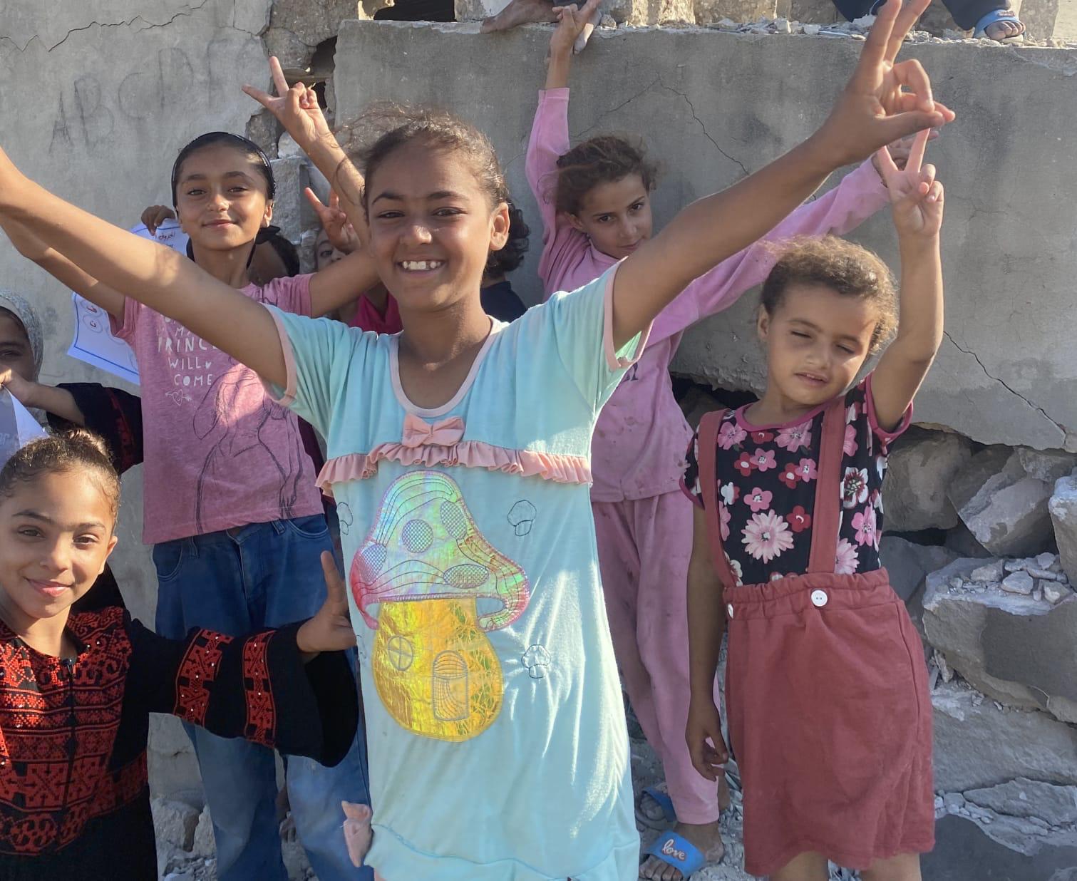 Girls making peace signs among the rubble